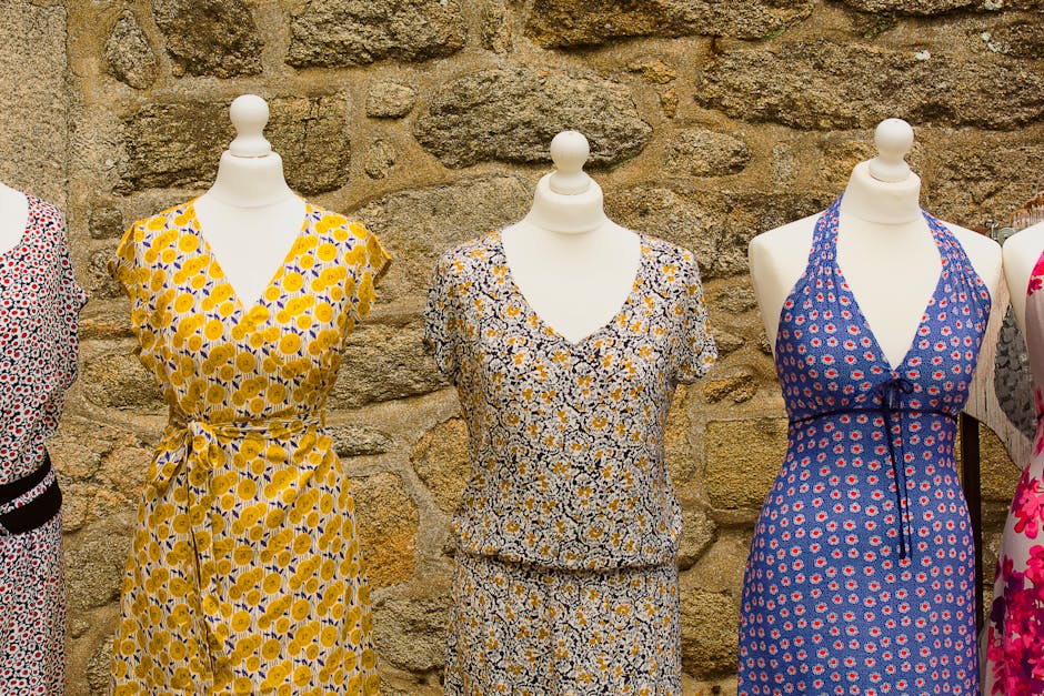 Vibrant floral dresses displayed on mannequins against a stone wall.